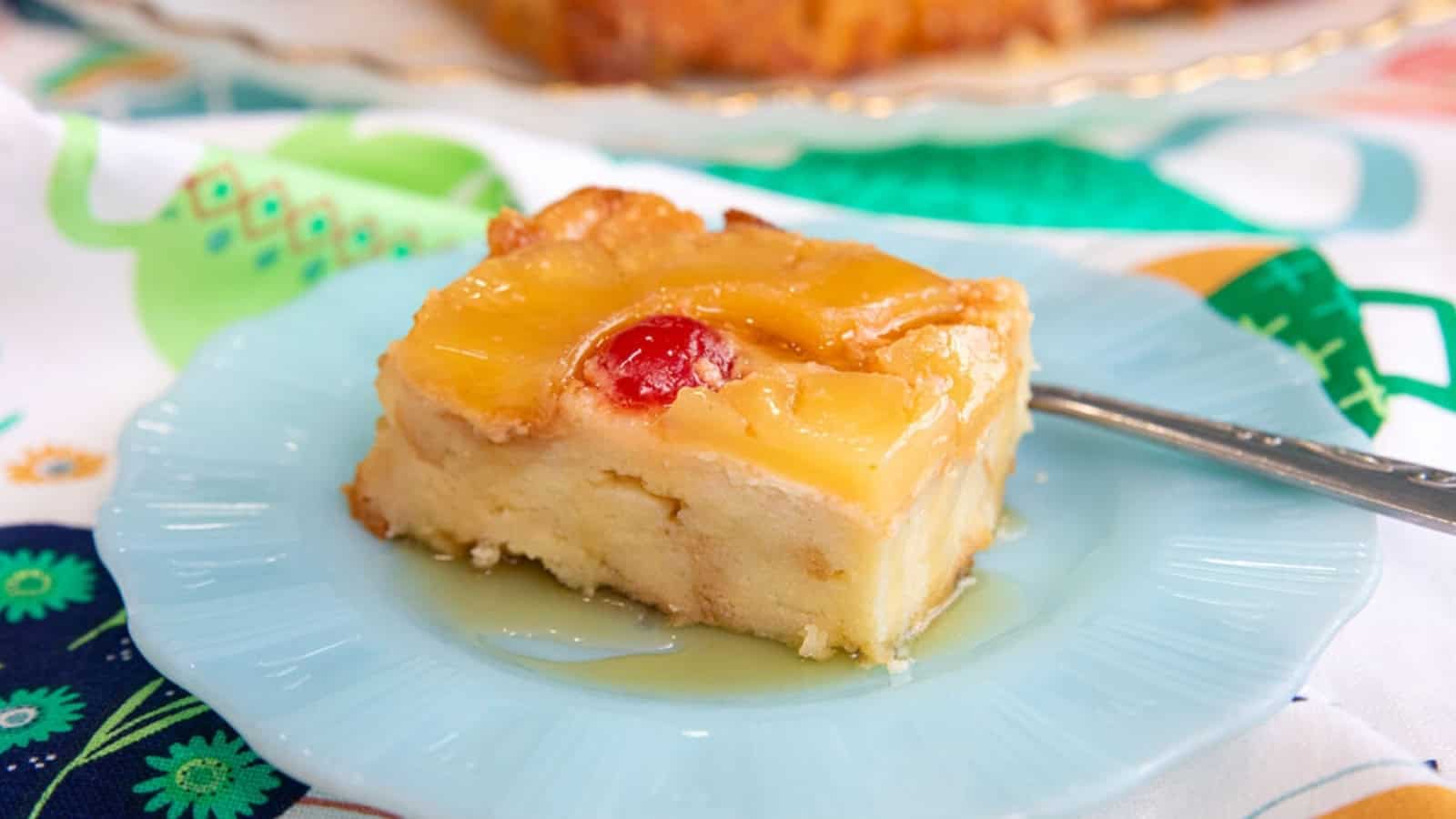 A slice of pineapple upside-down cake with a cherry on top, served on a light blue plate.