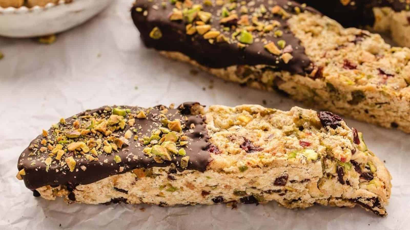 Biscotti dipped in chocolate and sprinkled with chopped pistachios on parchment paper.