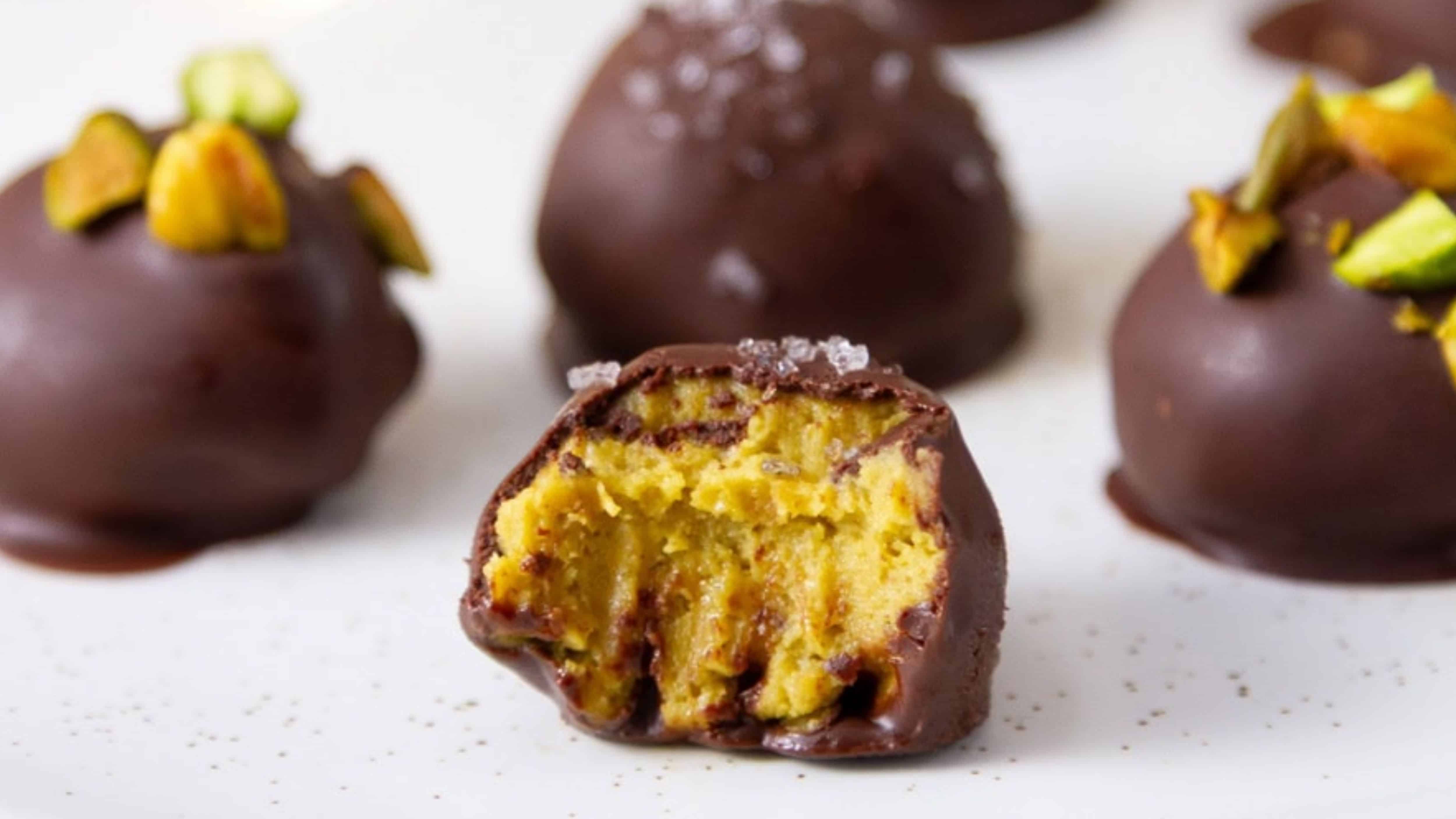 Chocolate-covered pumpkin spice truffles, one bitten, showing a crumbly, golden center and pistachio topping.