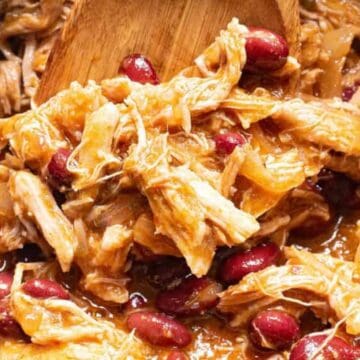 Shredded chicken and red kidney beans in a thick sauce being stirred with a wooden spoon.