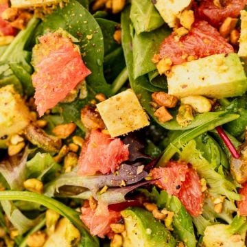 Close-up of a salad with leafy greens, avocado cubes, grapefruit pieces, and chopped nuts.