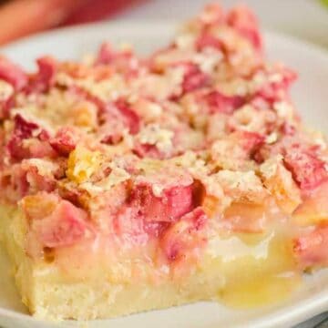 A square piece of rhubarb dessert bar with crumbly topping on a white plate.