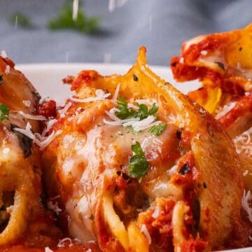 Three stuffed pasta shells topped with tomato sauce, melted cheese, parsley, and grated parmesan on a white plate.