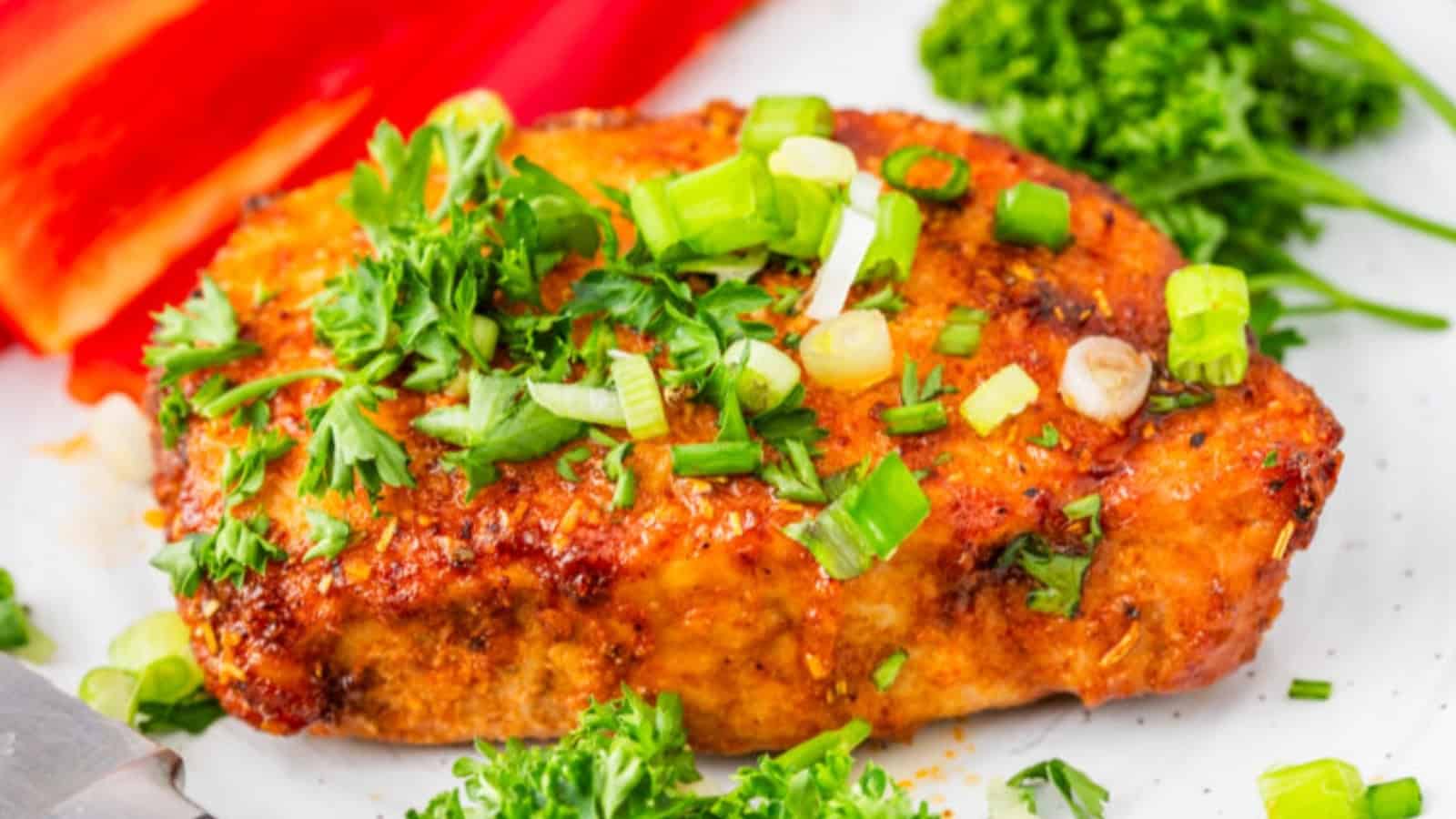 Seasoned grilled chicken breast garnished with chopped green onions and parsley, served with broccoli and red peppers.