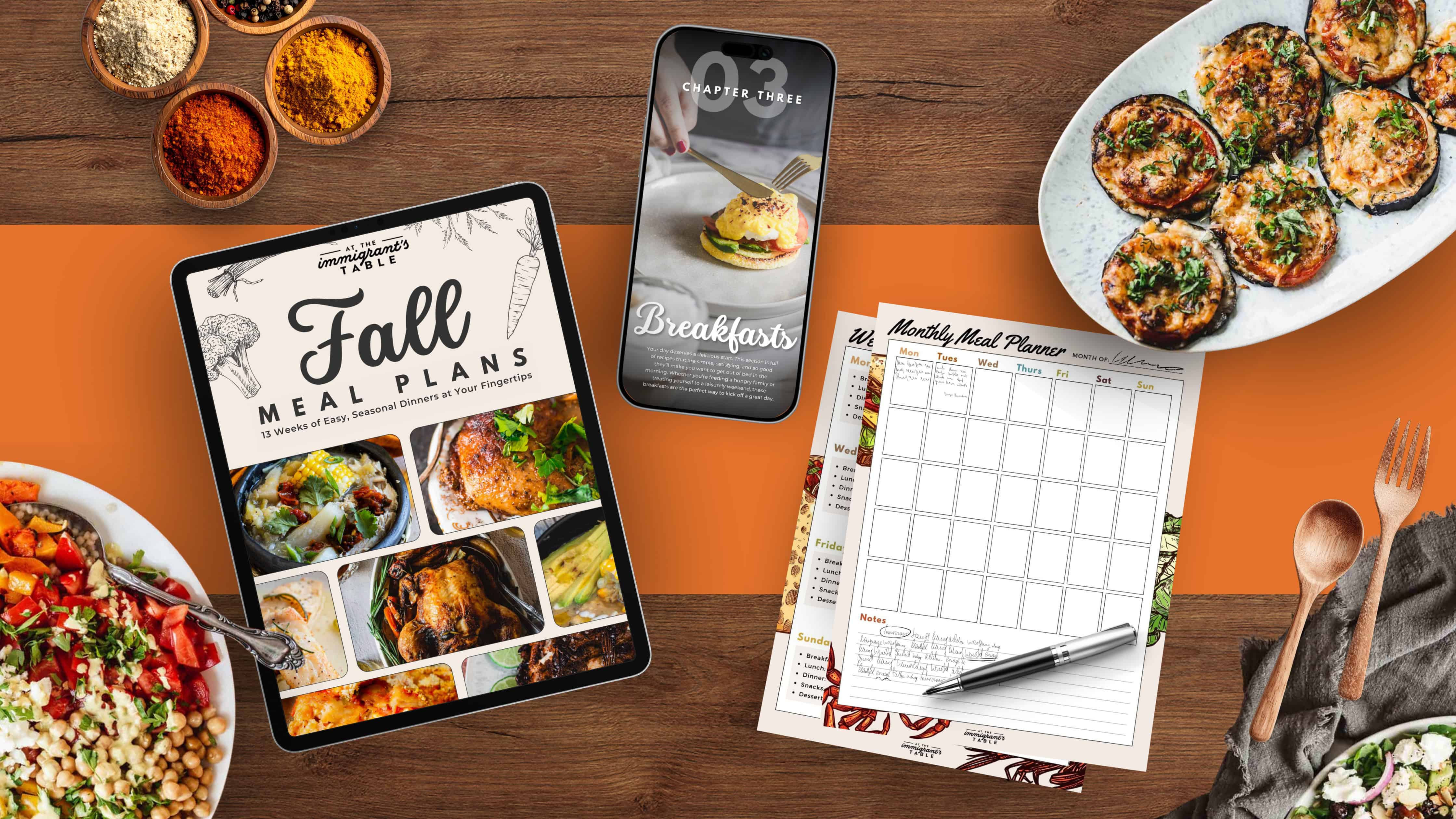 A tablet, phone, meal planner, and food dishes on a table with spices, featuring fall meal planning inspired by the immigrantstable shop.