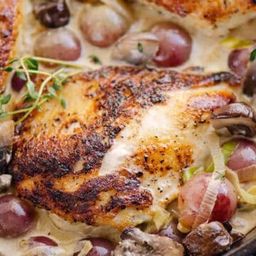 Seared chicken breasts in a creamy sauce with grapes, mushrooms, and herbs in a skillet.