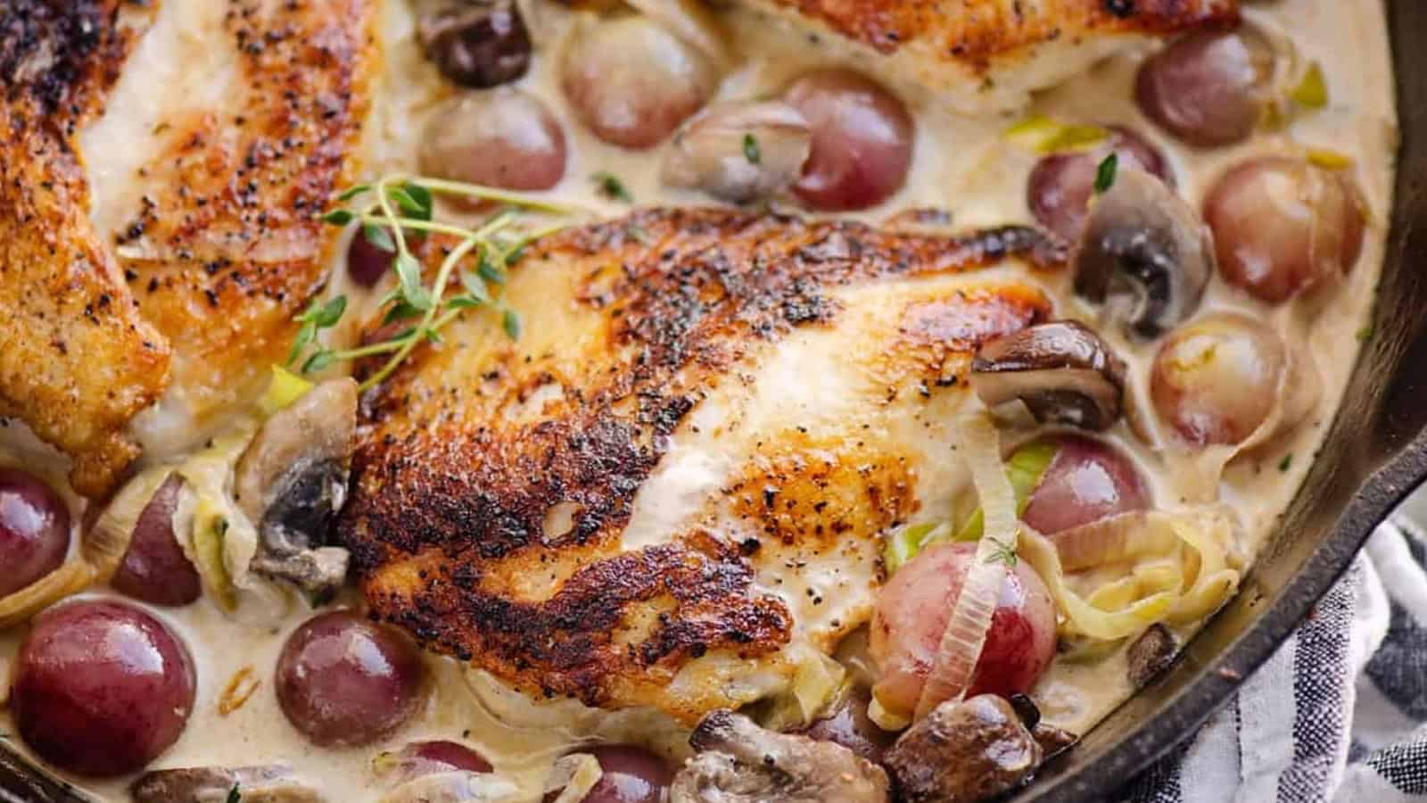Seared chicken breasts in a creamy sauce with grapes, mushrooms, and herbs in a skillet.