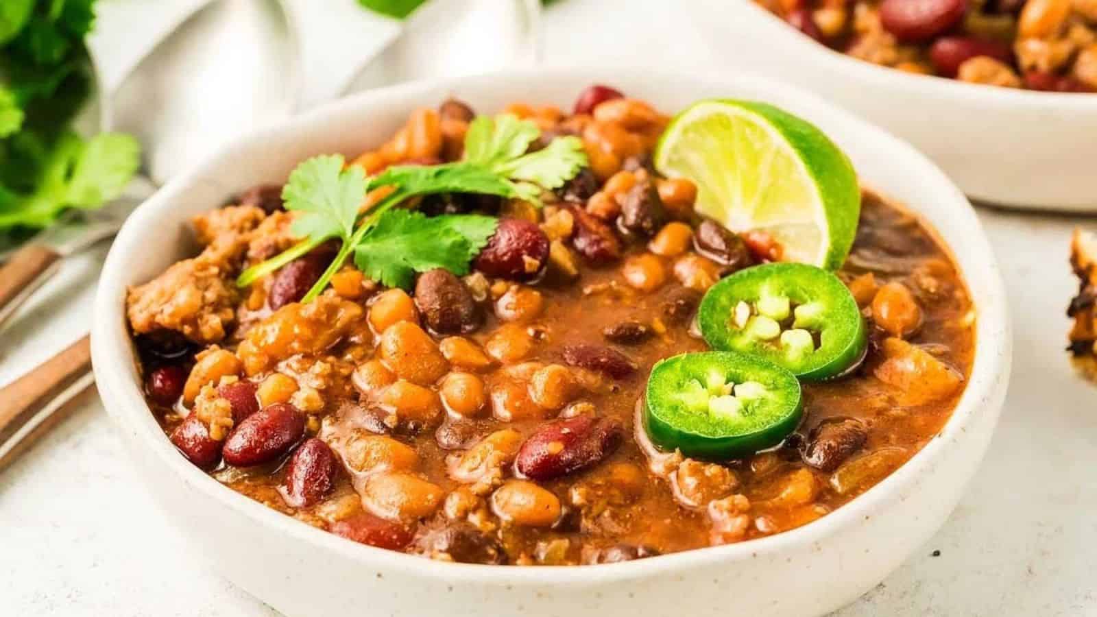 A bowl of chili with beans, ground meat, jalapeño slices, cilantro, and a lime wedge on top.