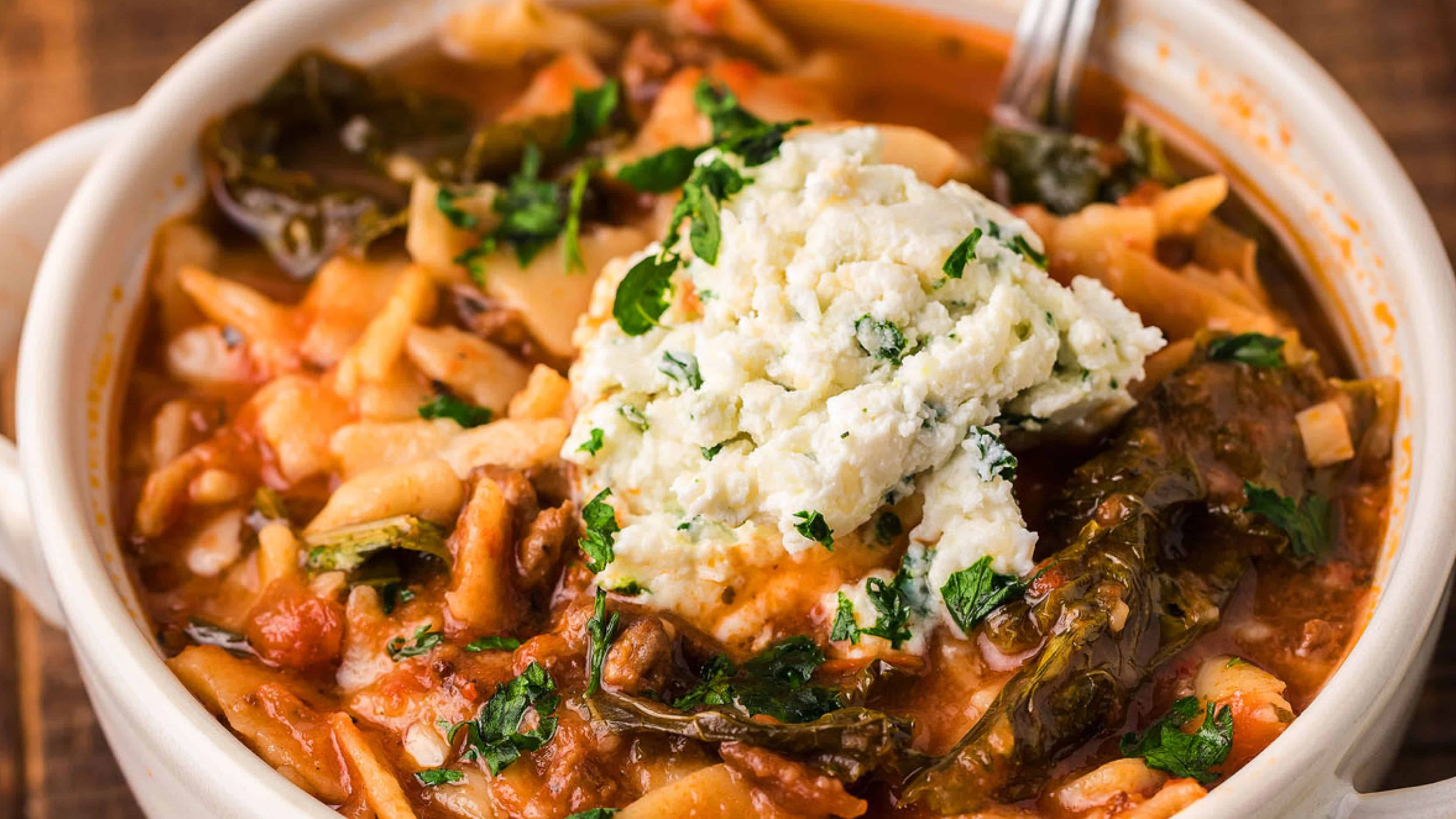 A bowl of vegetable soup topped with a dollop of ricotta cheese and sprinkled with fresh herbs.