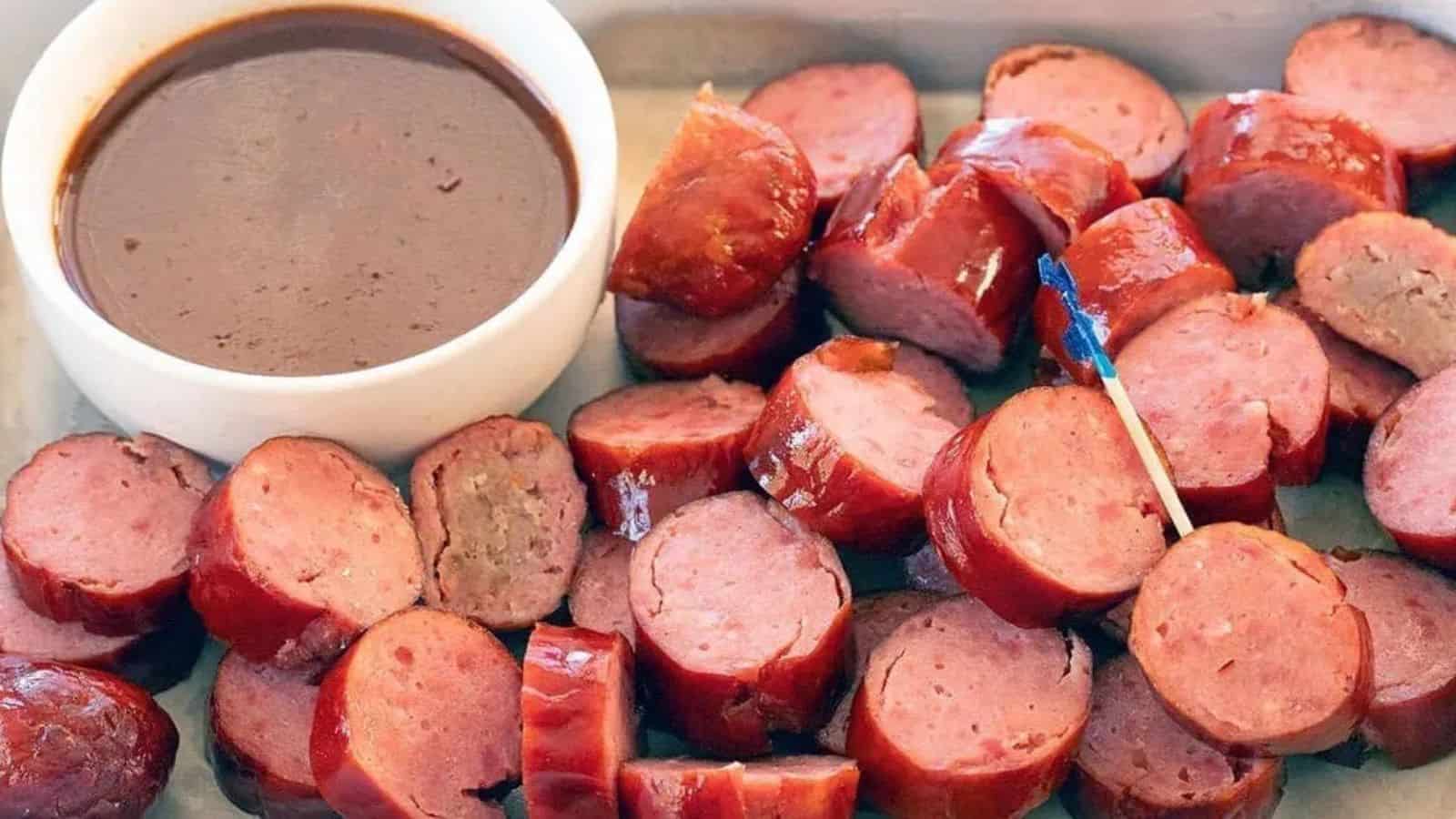 Sliced sausage pieces with a cup of brown dipping sauce and a toothpick on a tray.