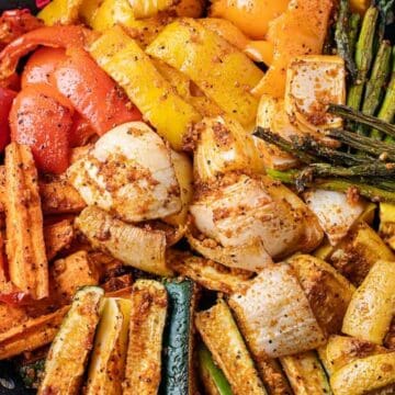A variety of seasoned, grilled vegetables including peppers, carrots, zucchini, asparagus, and onions on a platter.
