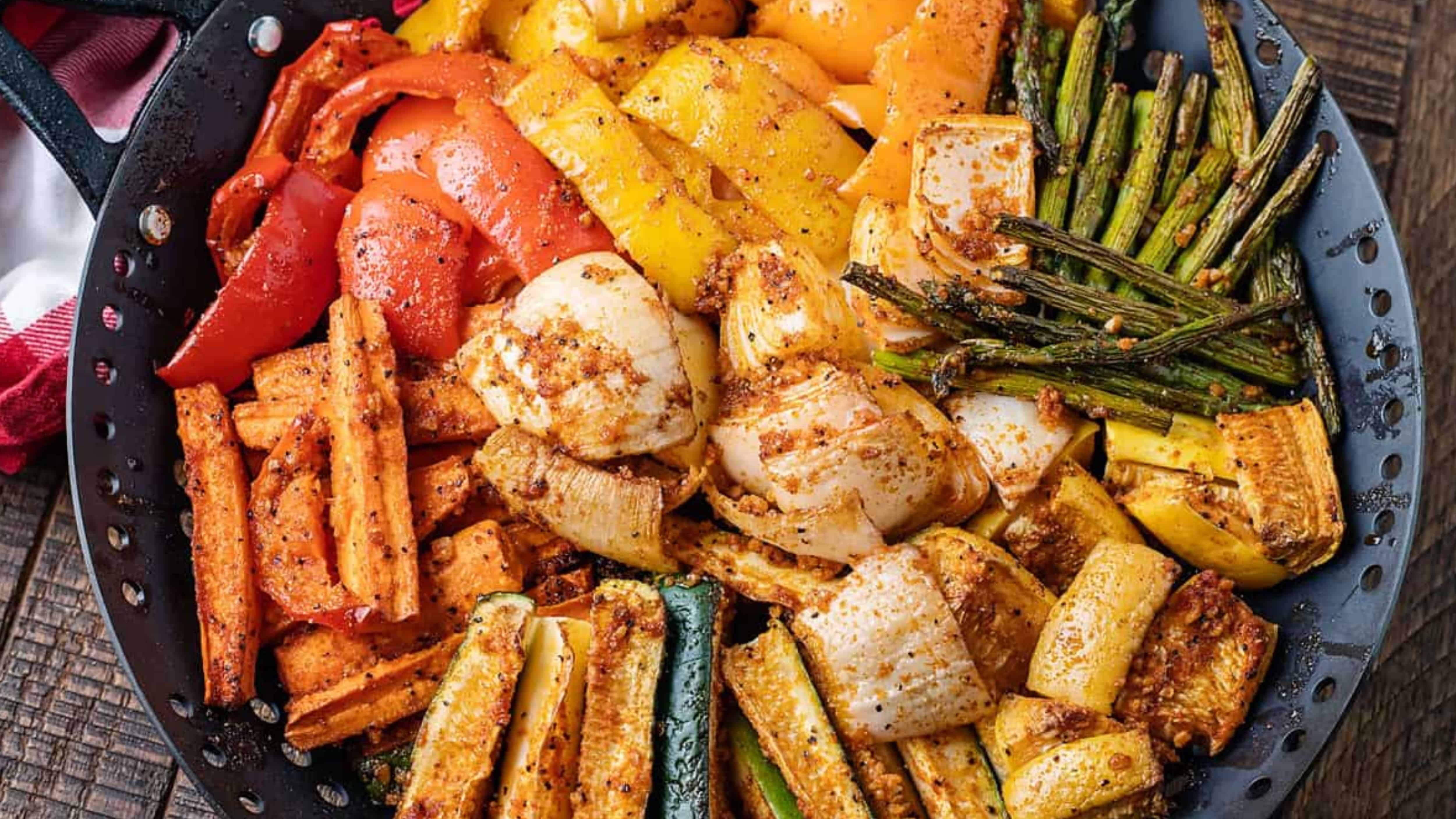 A variety of seasoned, grilled vegetables including peppers, carrots, zucchini, asparagus, and onions on a platter.