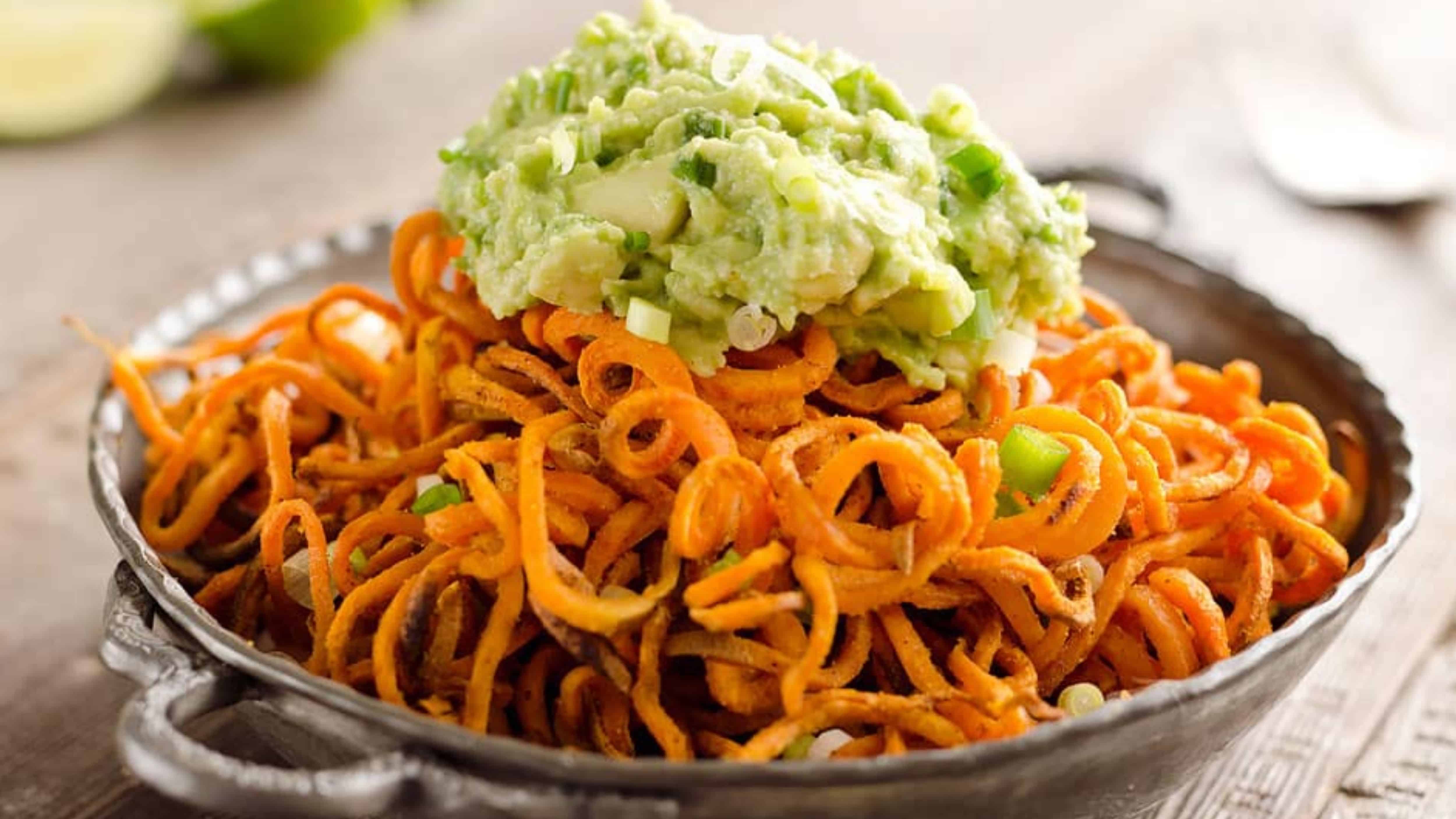 A plate of curly sweet potato fries topped with a generous scoop of guacamole.