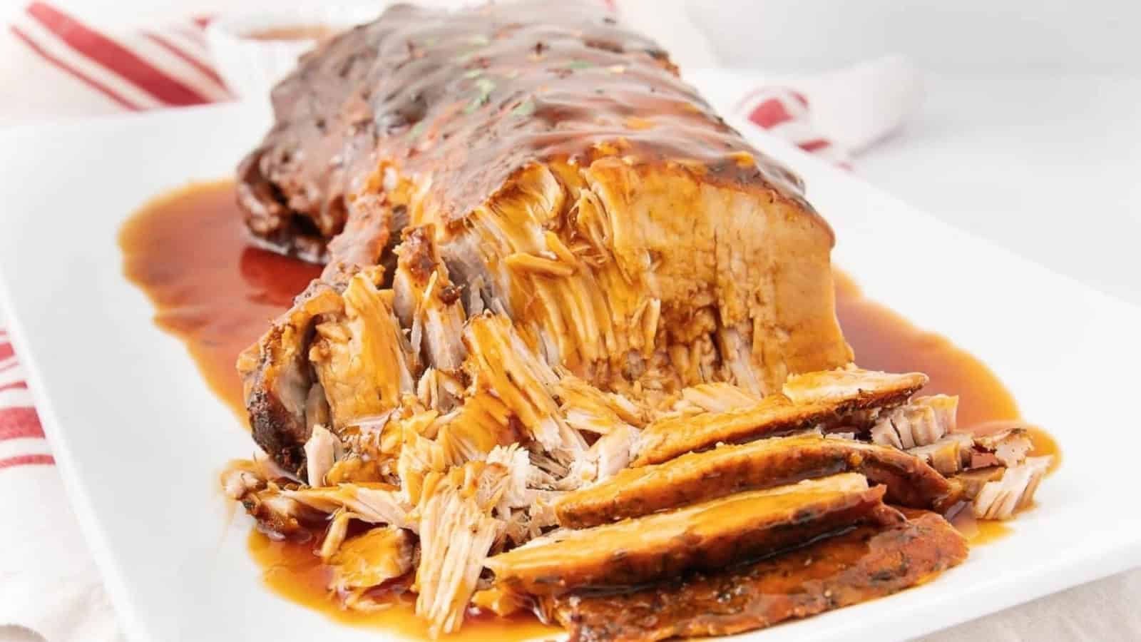 Sliced, juicy pot roast with gravy on a white platter, garnished with herbs and surrounded by sauce.
