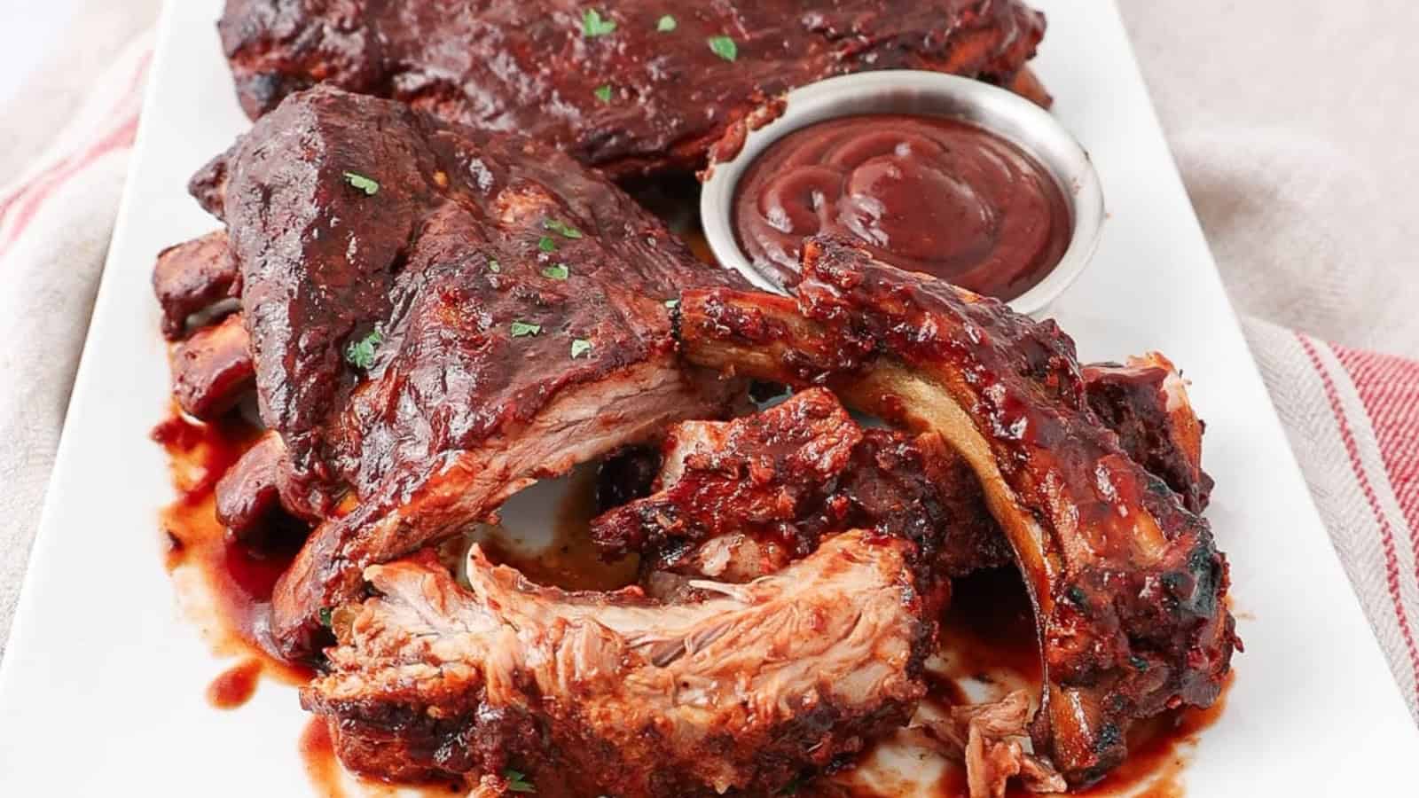 Barbecue ribs on a white plate with sauce, garnished with herbs, on a striped cloth background.
