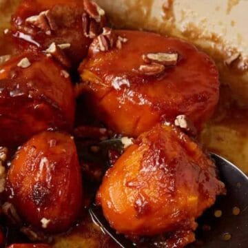 Candied yams topped with chopped pecans in a caramelized sauce, served in a dish with a slotted spoon.