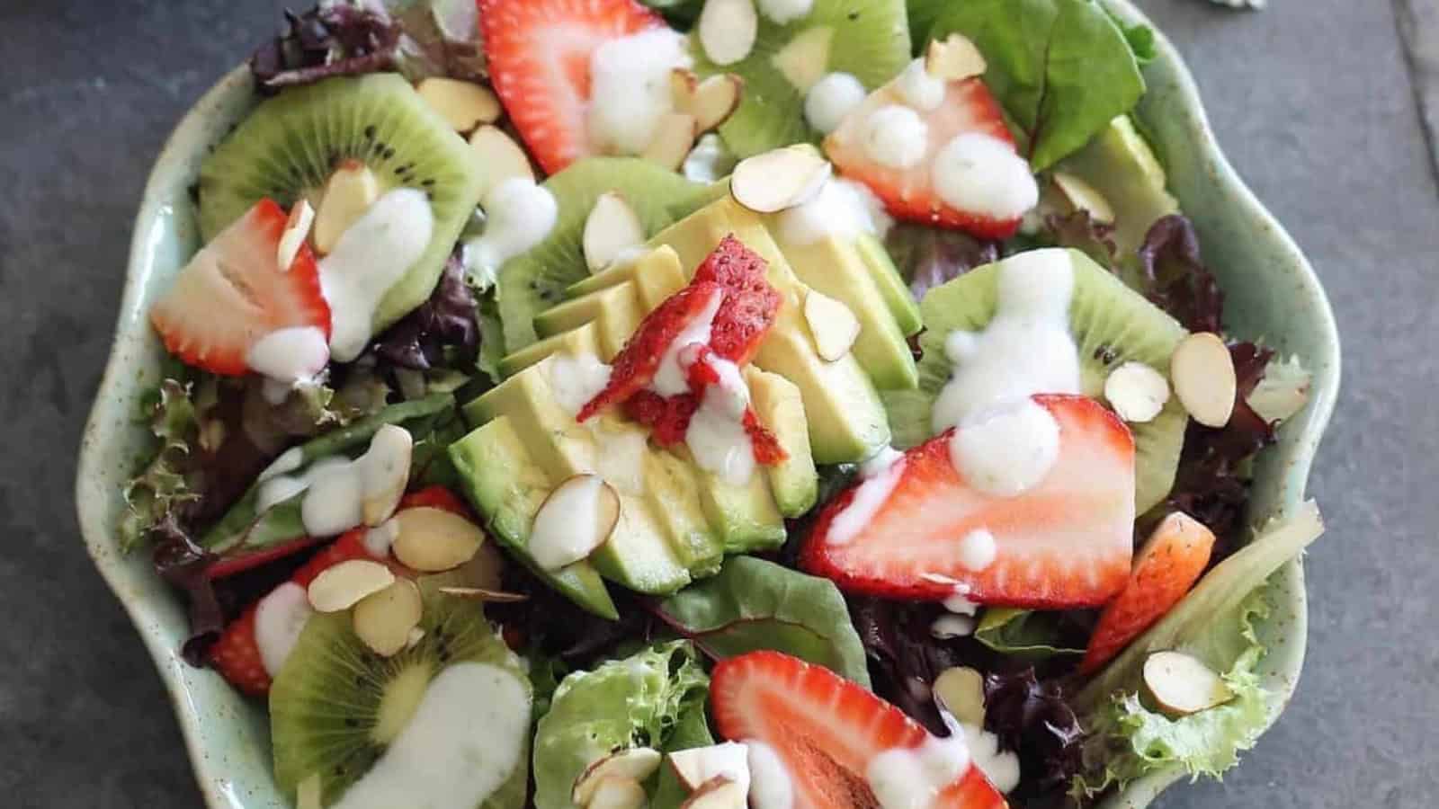 Salad with avocado, kiwi, strawberries, sliced almonds, and creamy dressing on a bed of leafy greens.