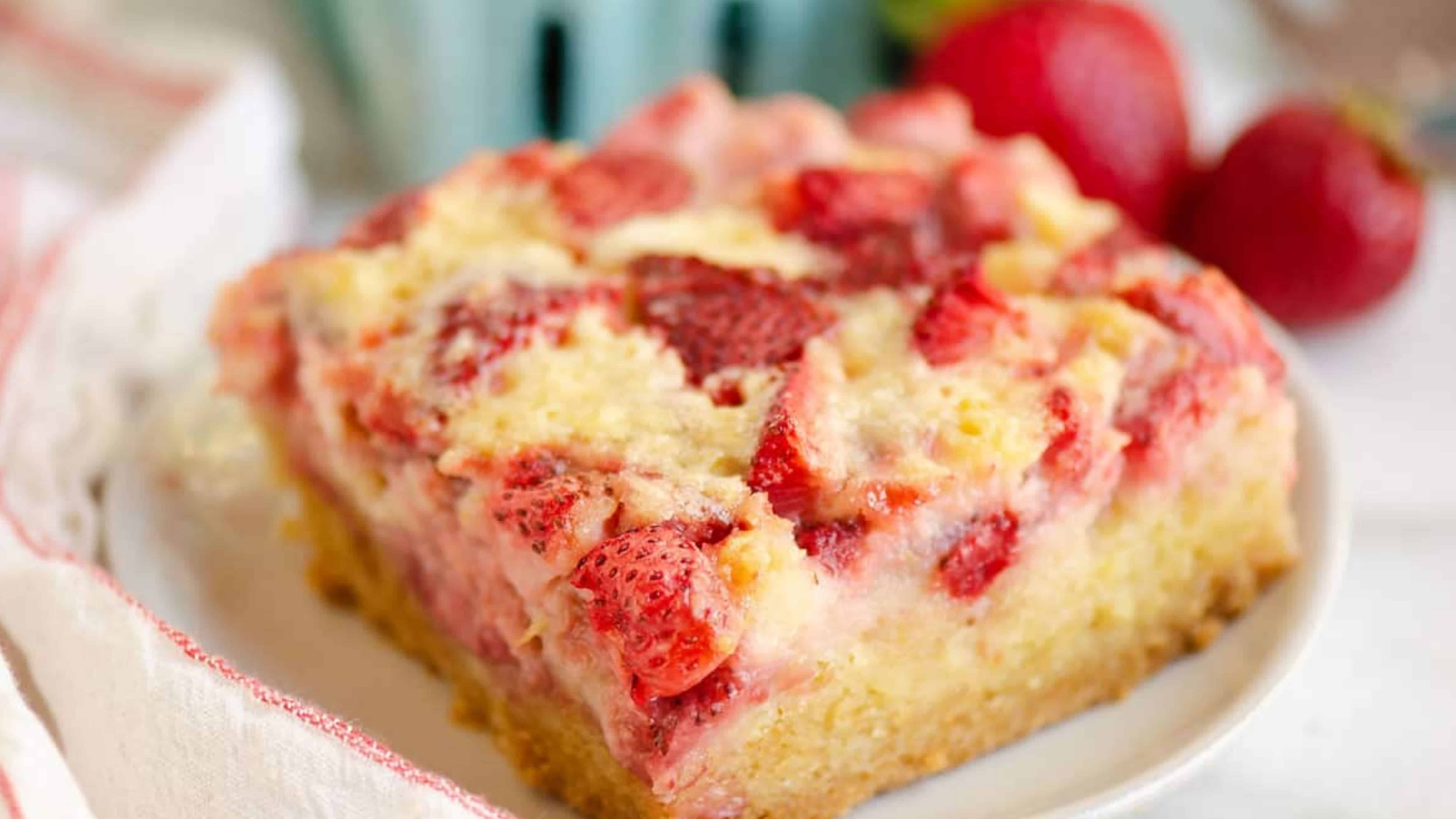 A slice of strawberry crumb cake with fresh strawberries on a white plate.