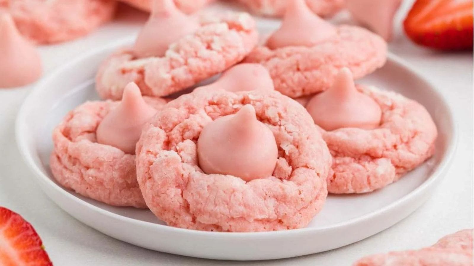 A plate of pink cookies topped with pink chocolate kisses, with strawberries nearby.