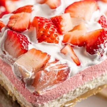 A slice of layered strawberry dessert with whipped cream, fresh strawberries, and a cookie crust.