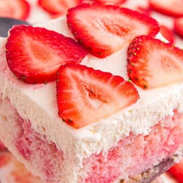 A slice of strawberry poke cake topped with whipped cream and fresh strawberry slices.