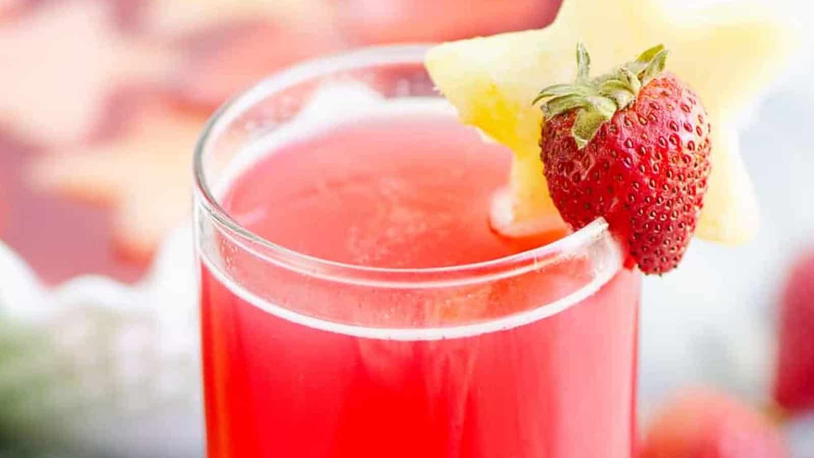 A glass of red juice garnished with a strawberry and a star-shaped fruit slice on the rim.