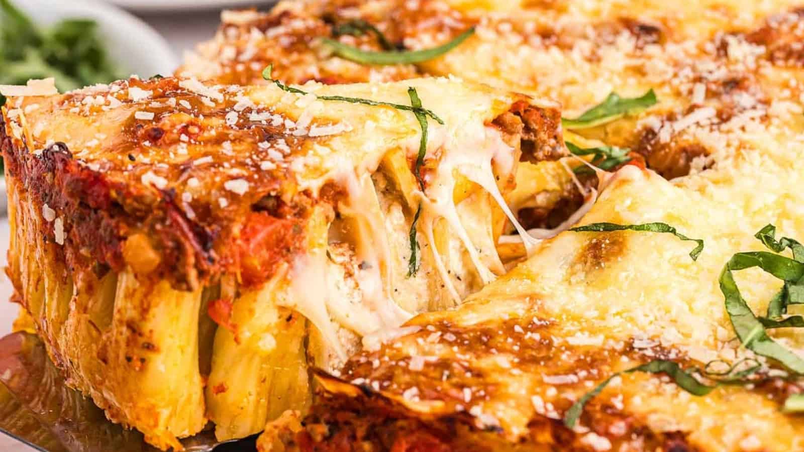 Cheesy baked pasta with tomato sauce, ground meat, and fresh basil being served from a casserole dish.