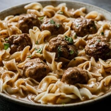 A bowl of egg noodles topped with meatballs in a brown gravy sauce, garnished with chopped herbs.