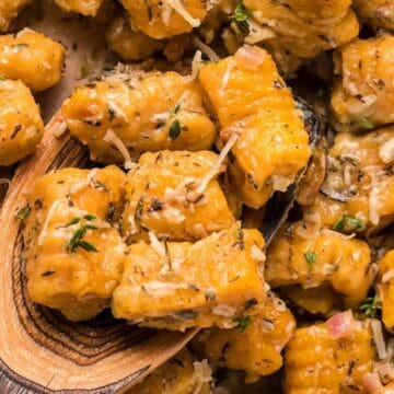 Close-up of seasoned gnocchi with herbs and grated cheese, with a wooden spoon scooping some pieces.