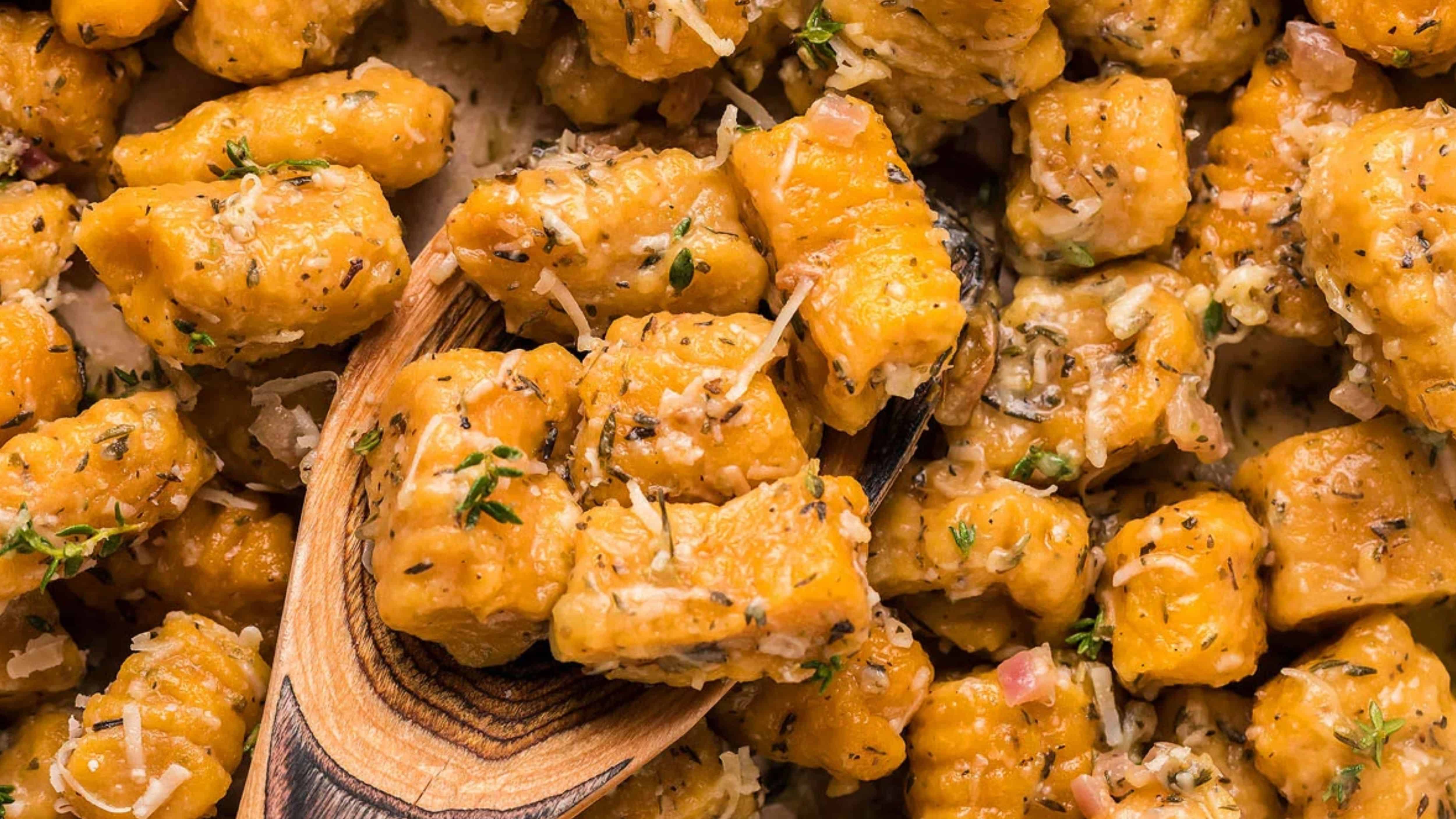 Close-up of seasoned gnocchi with herbs and grated cheese, with a wooden spoon scooping some pieces.