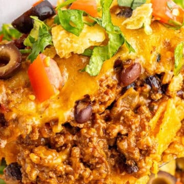 A close-up of a cheesy taco casserole with ground beef, black beans, olives, tomatoes, and chopped lettuce.