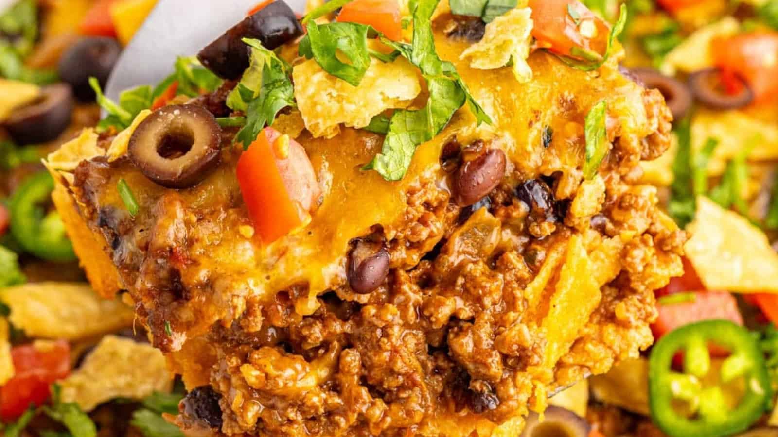 A close-up of a cheesy taco casserole with ground beef, black beans, olives, tomatoes, and chopped lettuce.