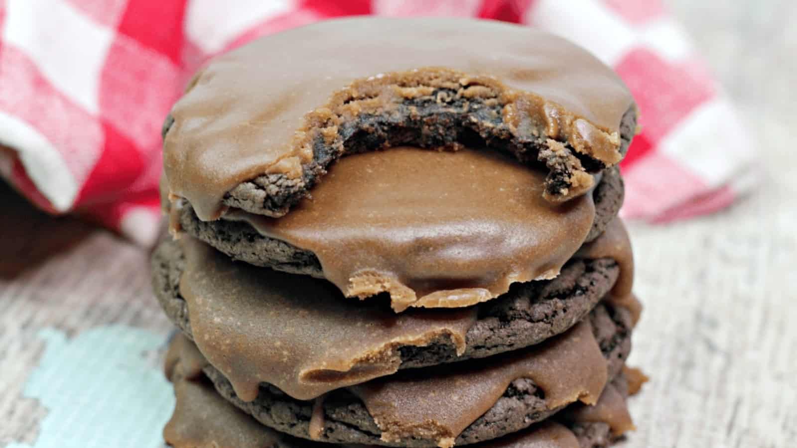 A stack of chocolate cookies with icing, the top cookie has a large bite taken out of it.