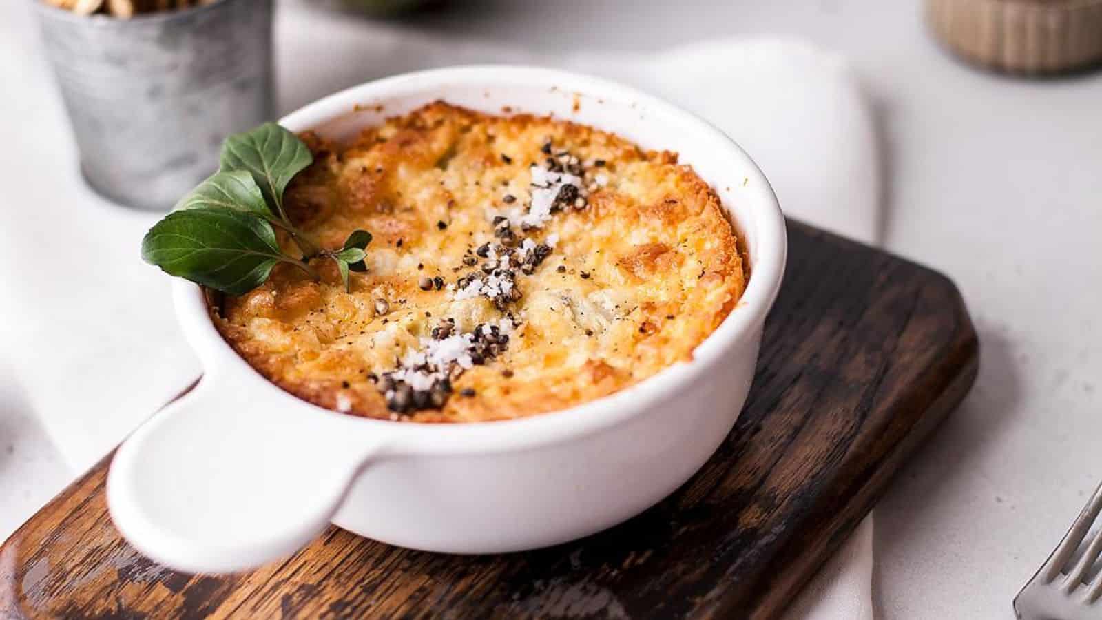 Baked casserole topped with herbs and grated cheese in a white dish on a wooden board.