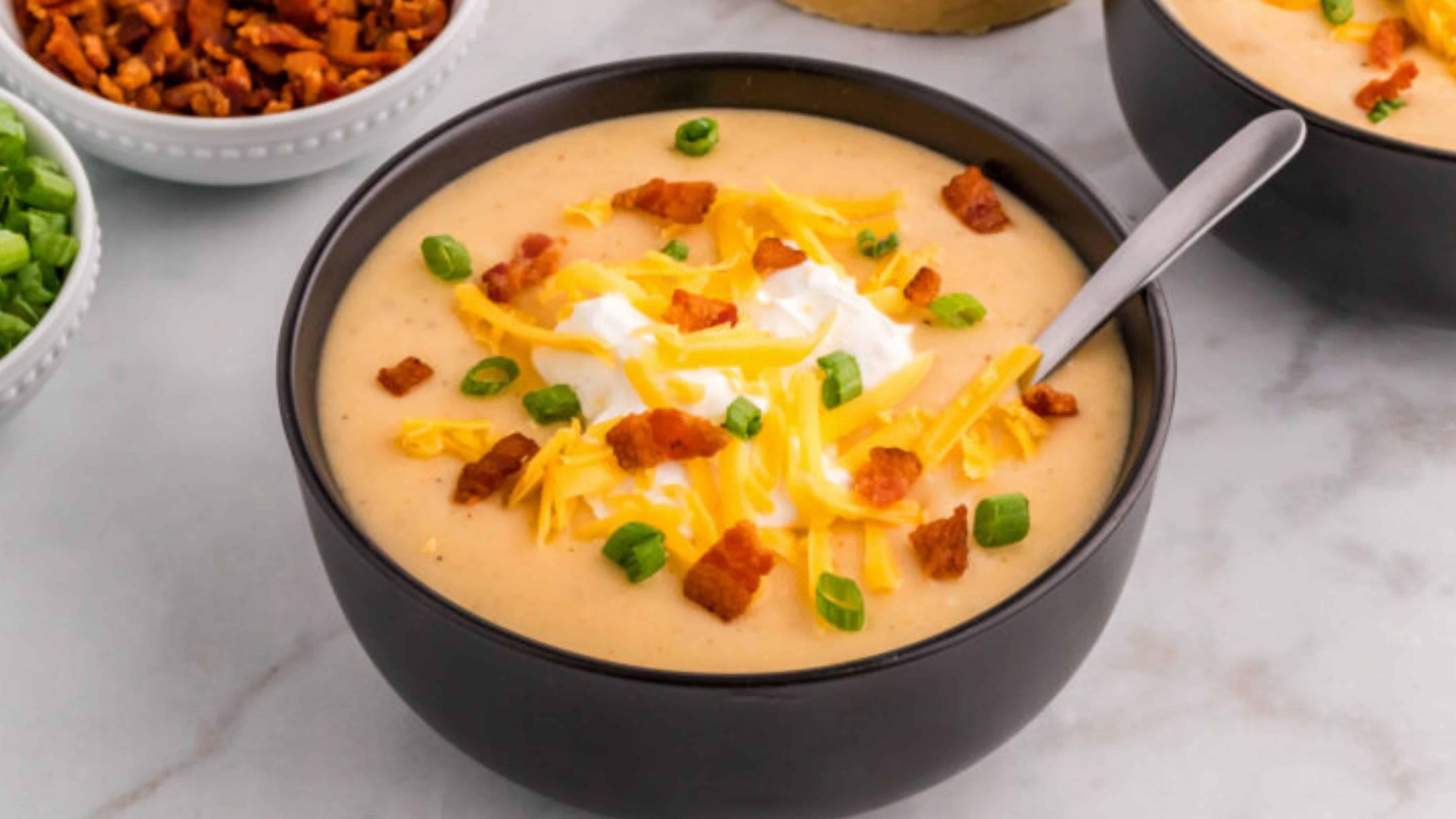 Bowl of creamy soup topped with shredded cheese, bacon bits, green onions, and a dollop of sour cream.