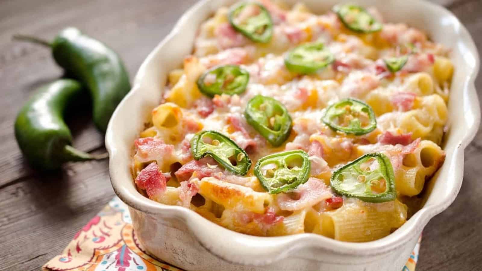 Baked pasta in a casserole dish topped with melted cheese, bacon, and sliced jalape&ntilde;os; two jalape&ntilde;os beside.
