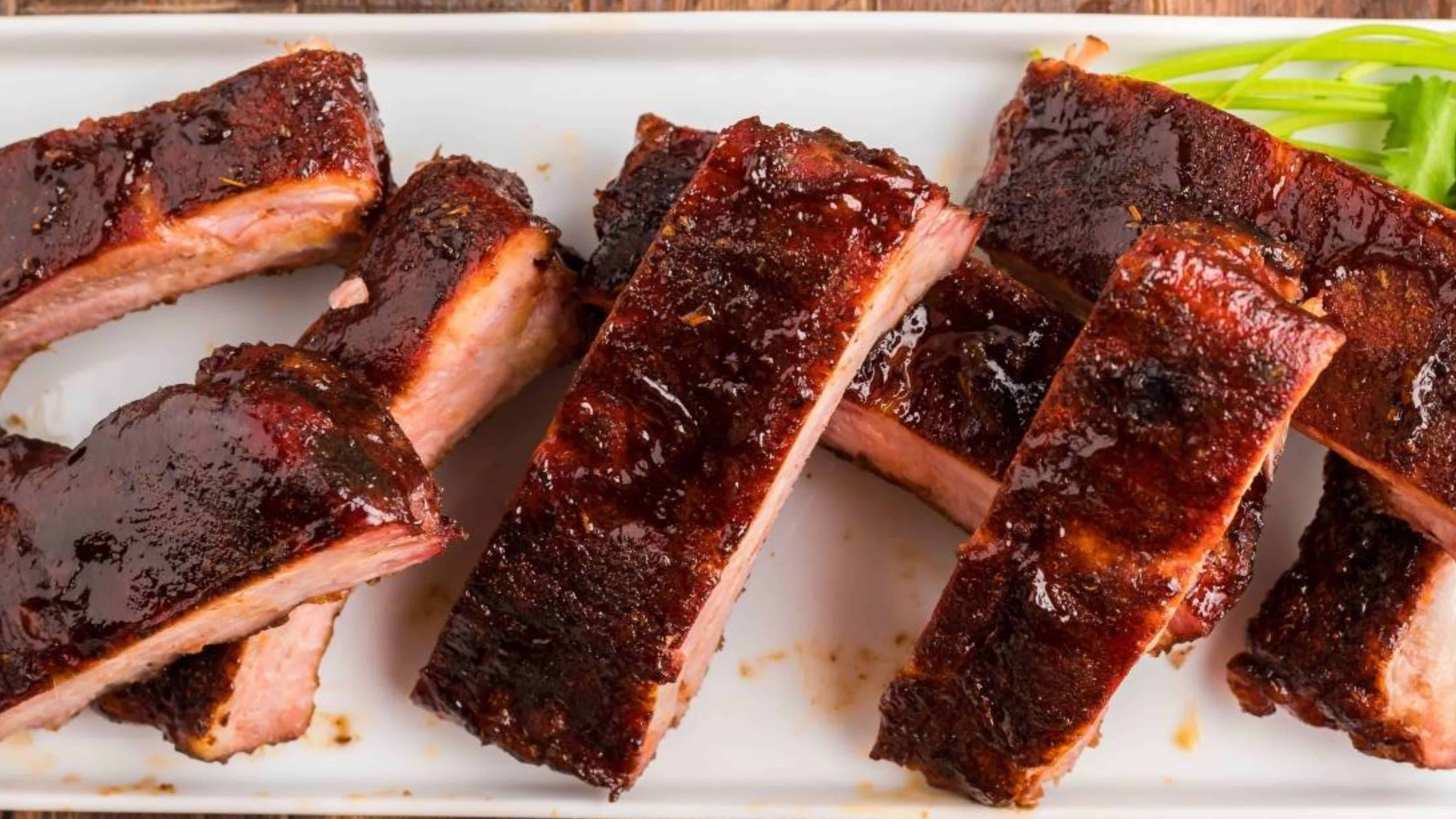 Barbecue pork ribs with a dark, glossy glaze served on a white rectangular plate with a garnish.