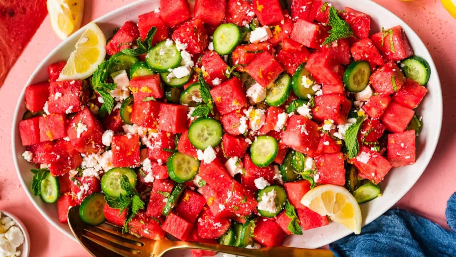 Watermelon, cucumber, mint, and feta salad on a white platter, garnished with lemon wedges.