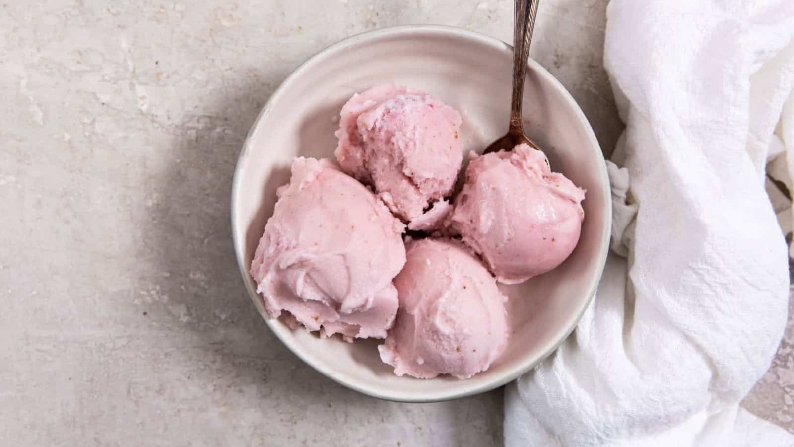 3-Ingredient Keto Strawberry Ice Cream in glass jar with an ice cream scoop and in a white bowl with a spoon.