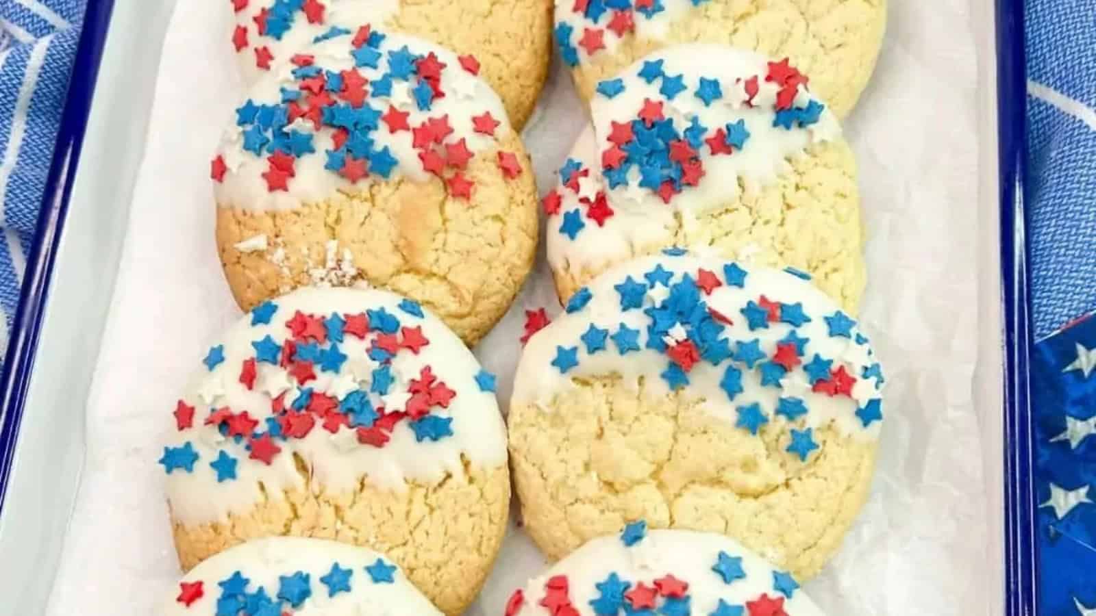 Round cookies half-dipped in white icing with red and blue star sprinkles, arranged on a tray.