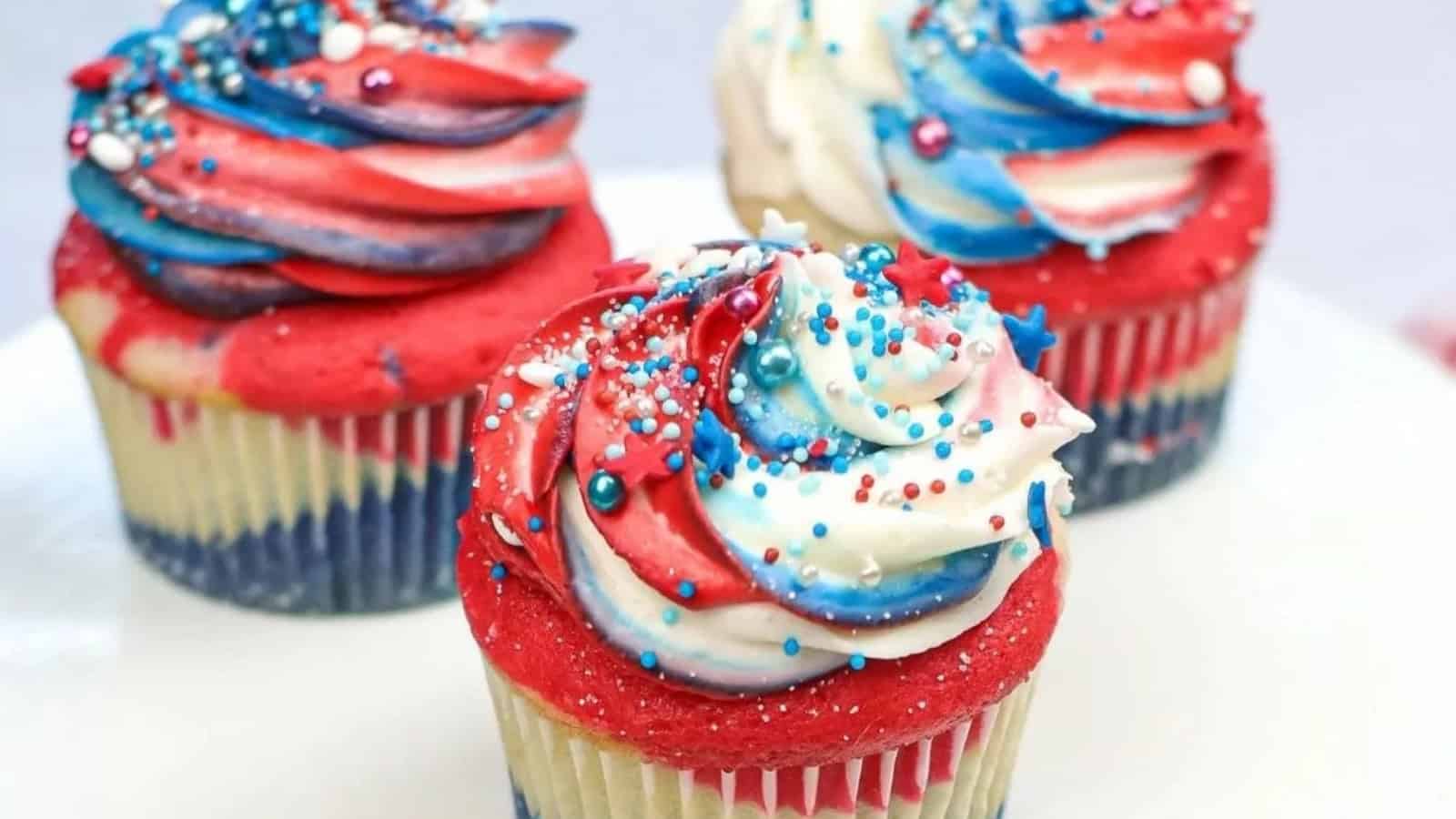 Cupcakes with red, white, and blue swirled frosting and sprinkles, arranged on a white plate.