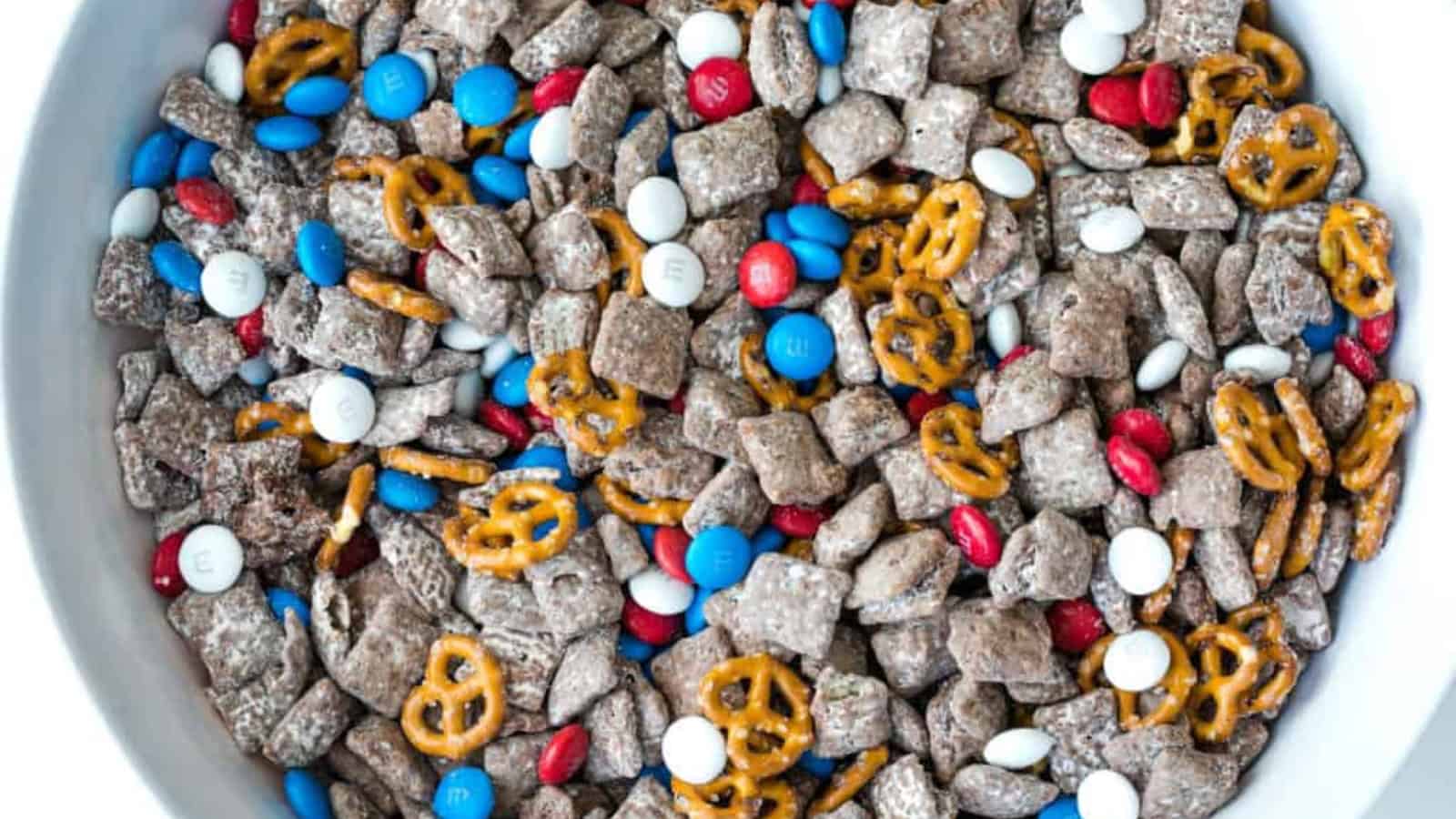 A bowl of snack mix with chocolate puppy chow, pretzels, and red, white, and blue M&Ms.