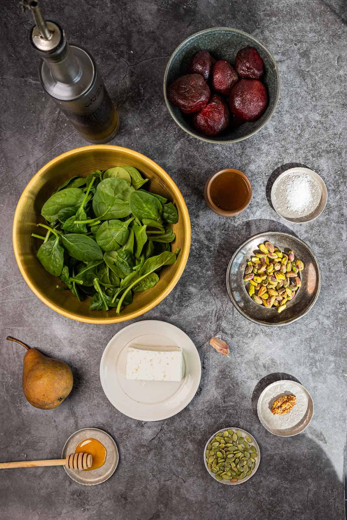Flat lay of salad ingredients: spinach, poached beets, pear, feta, pistachios, pepitas, oil, honey, and seasonings.