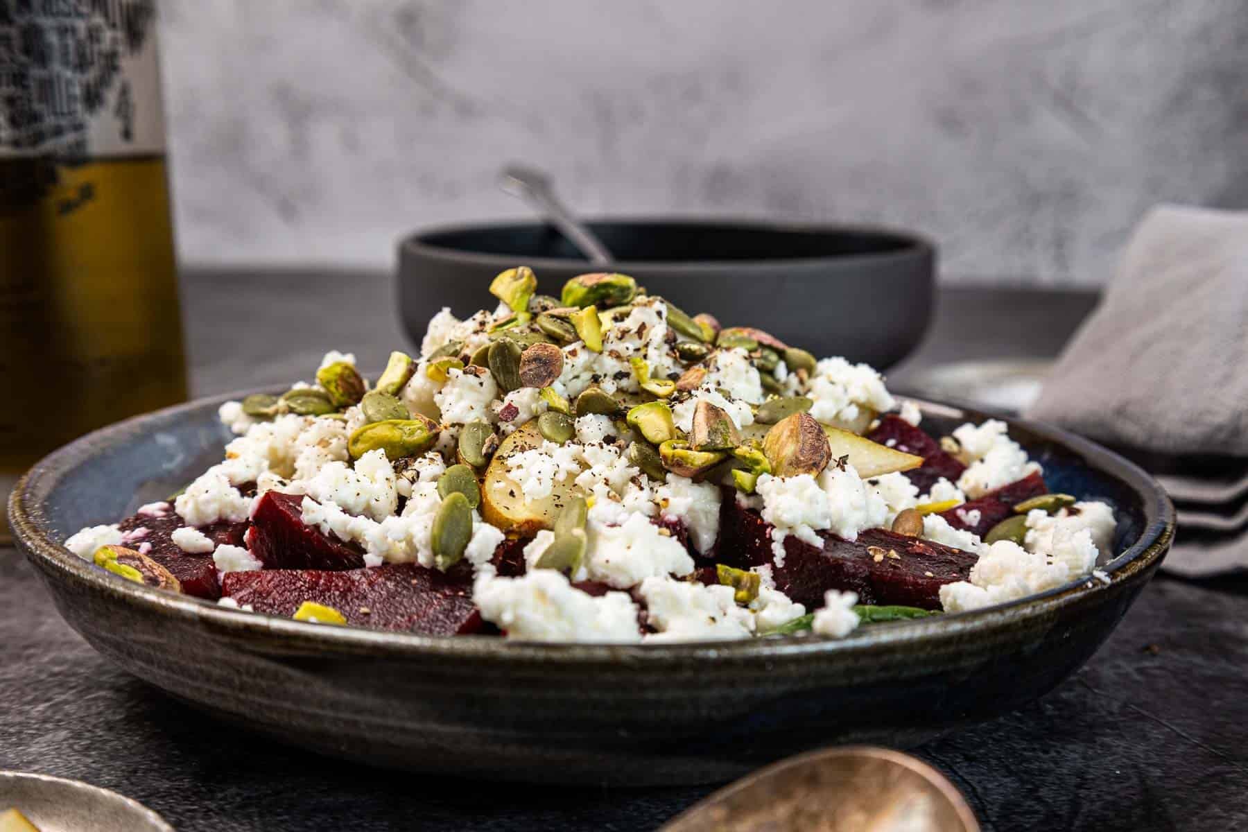 A plate of beet salad topped with crumbled cheese and pistachios, served on a dark table.