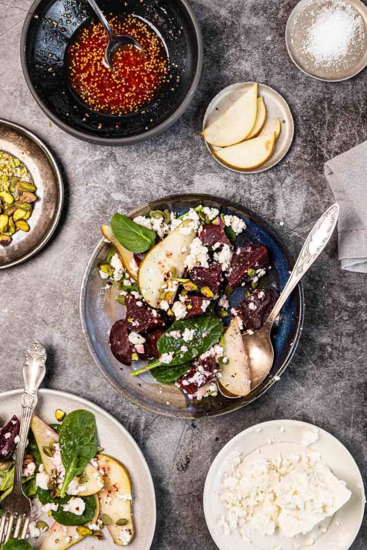 Overhead view of a beet, spinach, and pear salad with feta cheese and dressing on a gray tabletop.