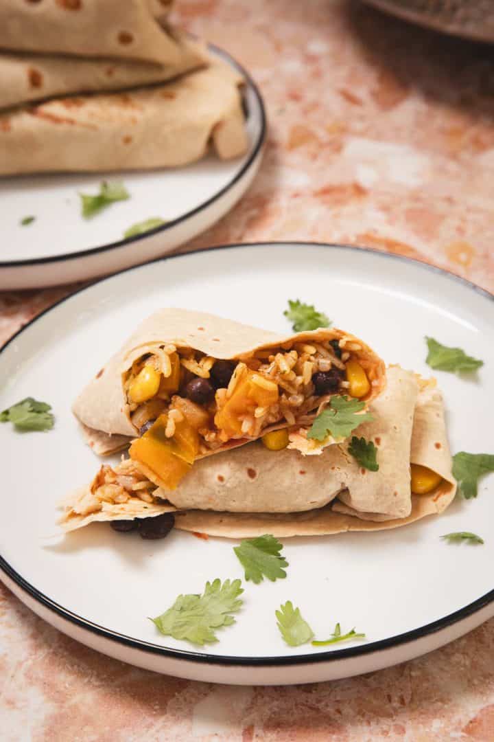 A burrito filled with rice, beans, corn, and veggies, garnished with fresh cilantro on a white plate.