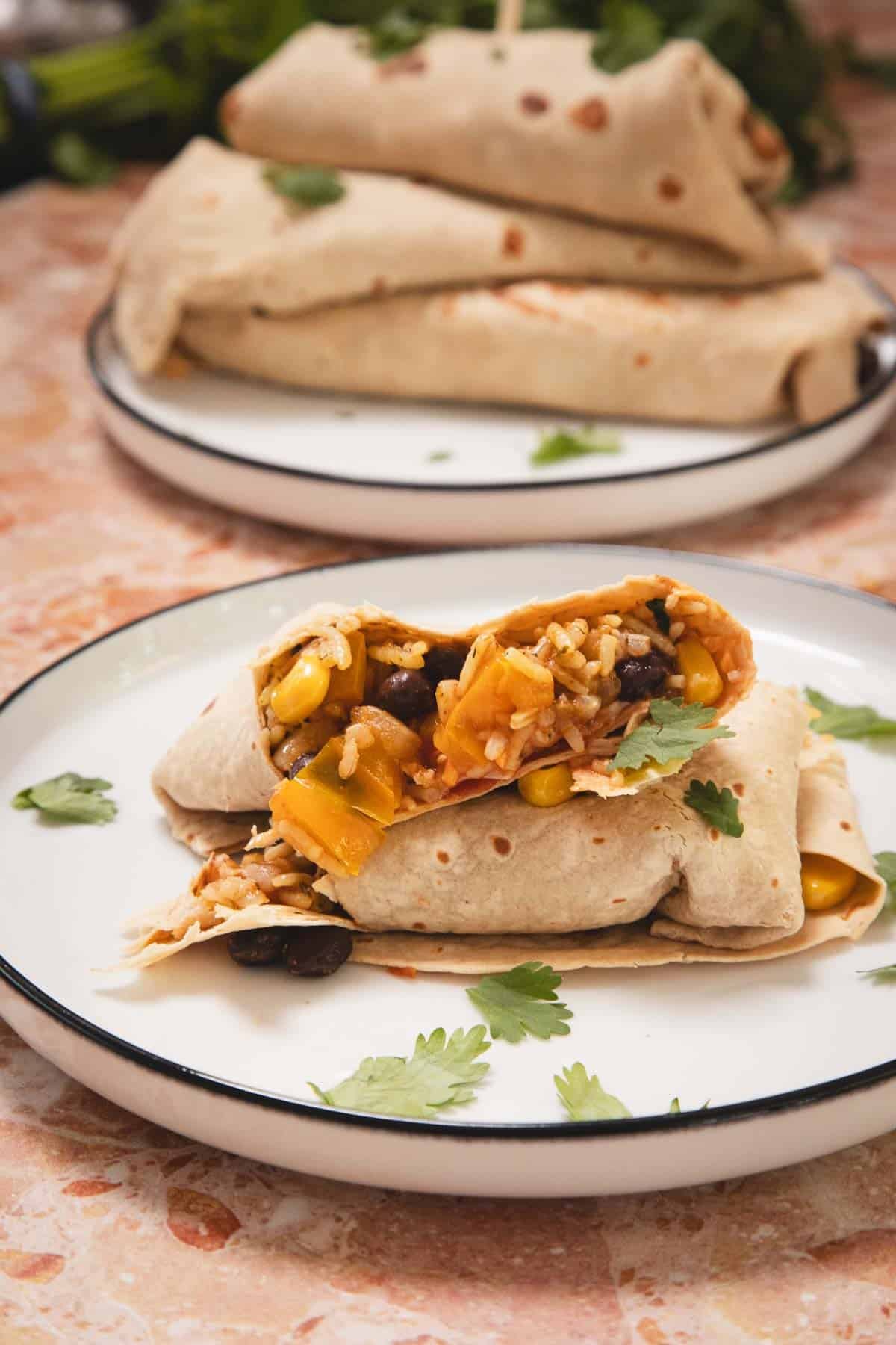 A plate with a cut burrito filled with rice, beans, corn, and vegetables, garnished with cilantro.
