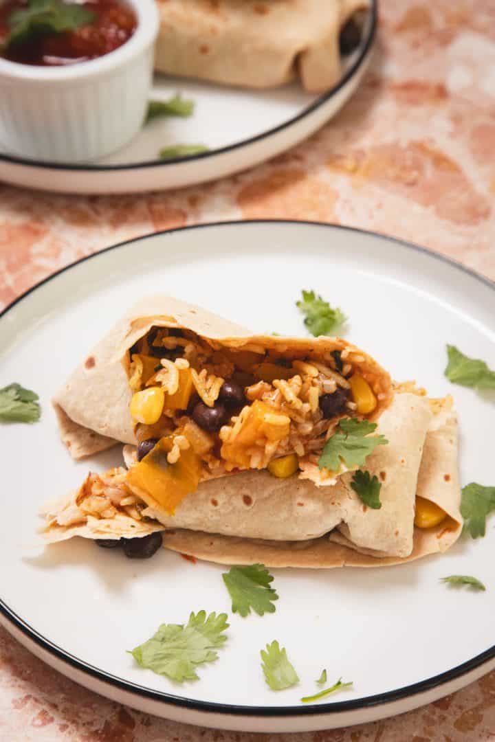 A burrito filled with rice, beans, corn, and veggies on a plate, garnished with cilantro.