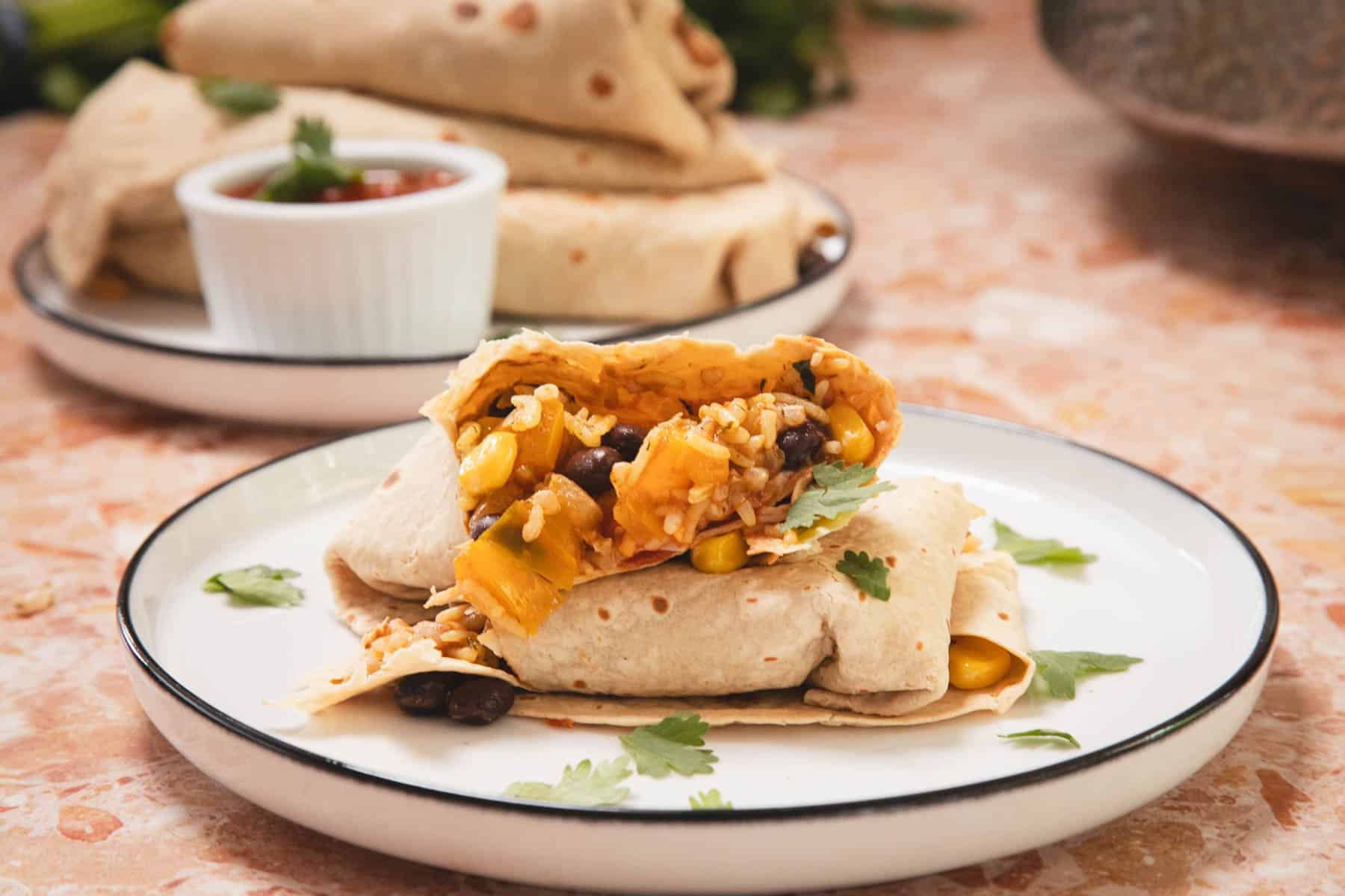 A burrito filled with rice, beans, corn, and vegetables sits on a plate, garnished with cilantro.