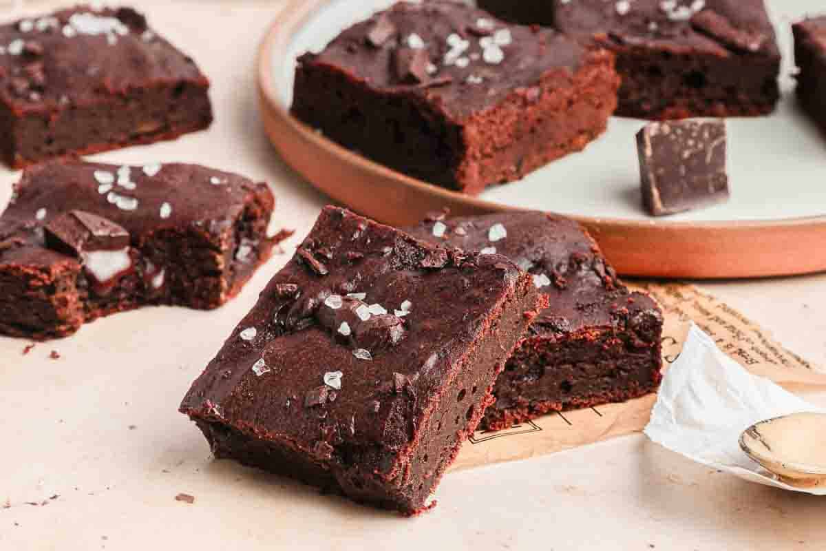 Fudgy chocolate brownies topped with sea salt flakes, arranged on a light surface and a round plate.